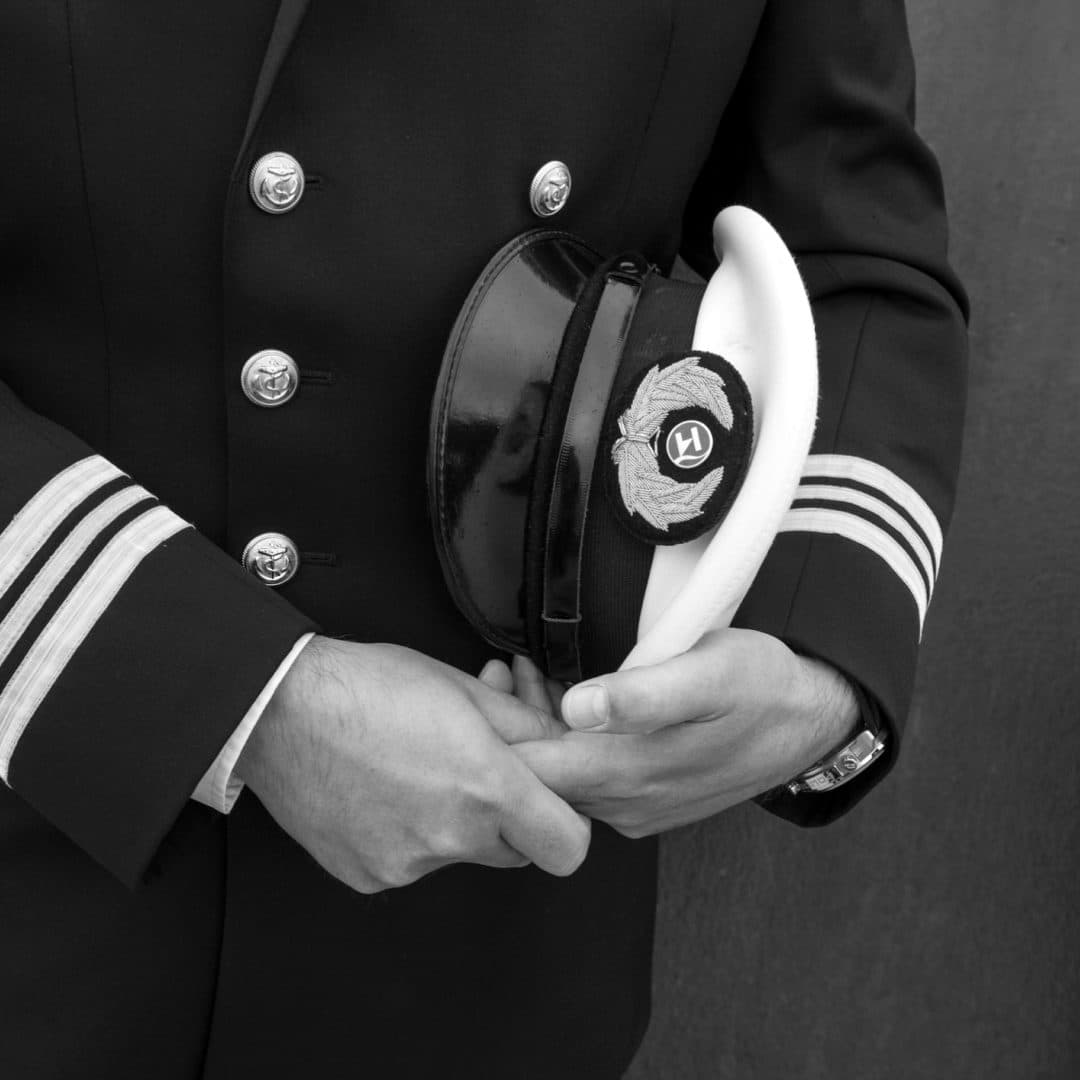 Een kapitein in uniform houdt zijn pet vast